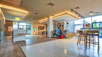 Eine geräumige Lobby mit einer Rezeption, einer Sitzecke und großen Fenstern, die natürliches Licht hereinlassen.