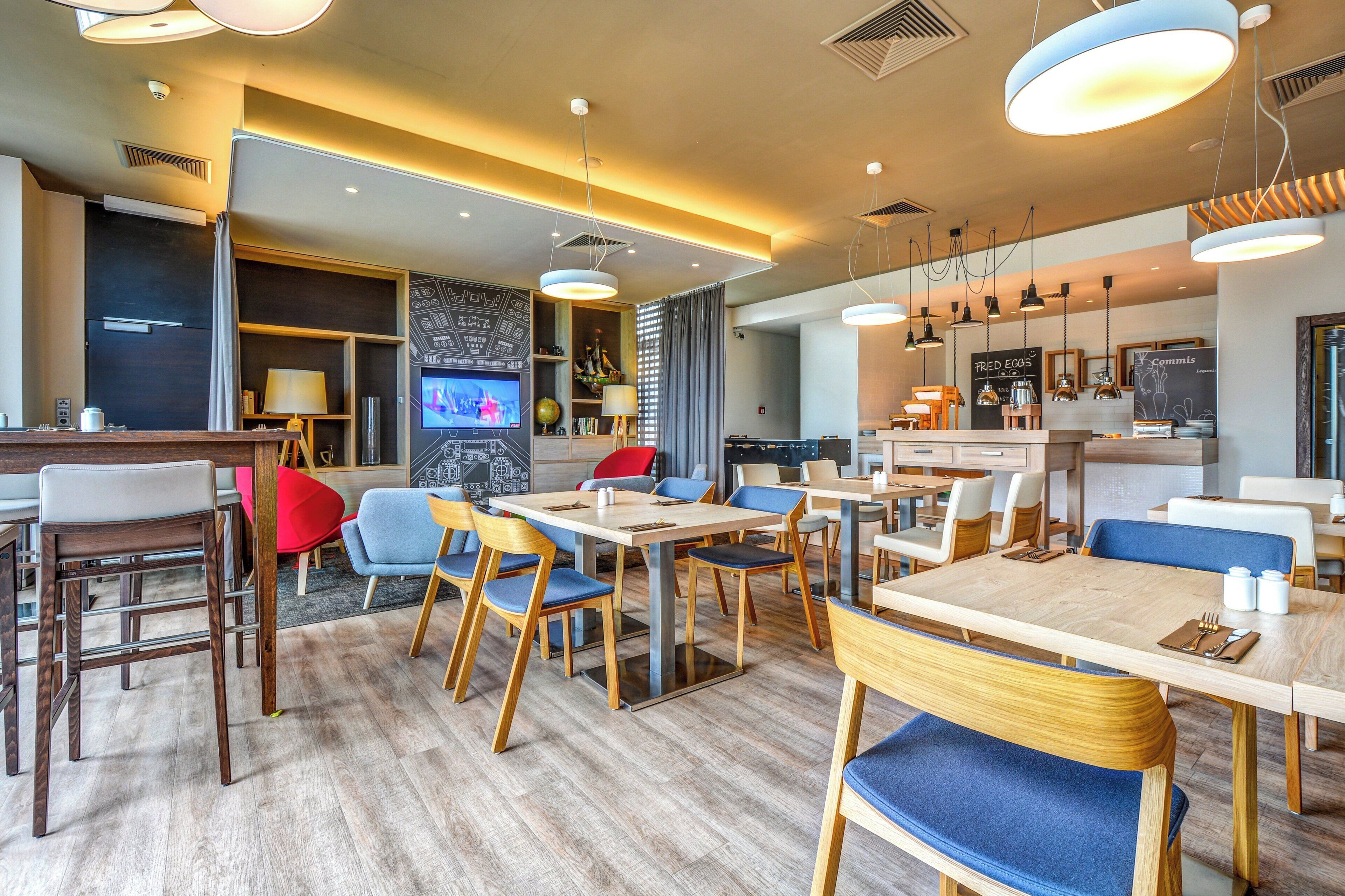 Een modern restaurantinterieur met houten tafels en stoelen, een televisie en een schoolbord met de menukaart.
