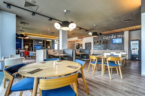 A modern restaurant with round tables, blue upholstered chairs, and a large screen displaying a menu.