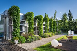 A modern building with large glass windows, a wooden deck, and a garden area with potted plants and a seating arrangement. - Holiday Inn Prague Airport by IHG (Prague)