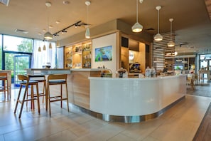 A modern bar area with a curved counter, wooden stools, and pendant lighting. - Holiday Inn Prague Airport by IHG (Prague)