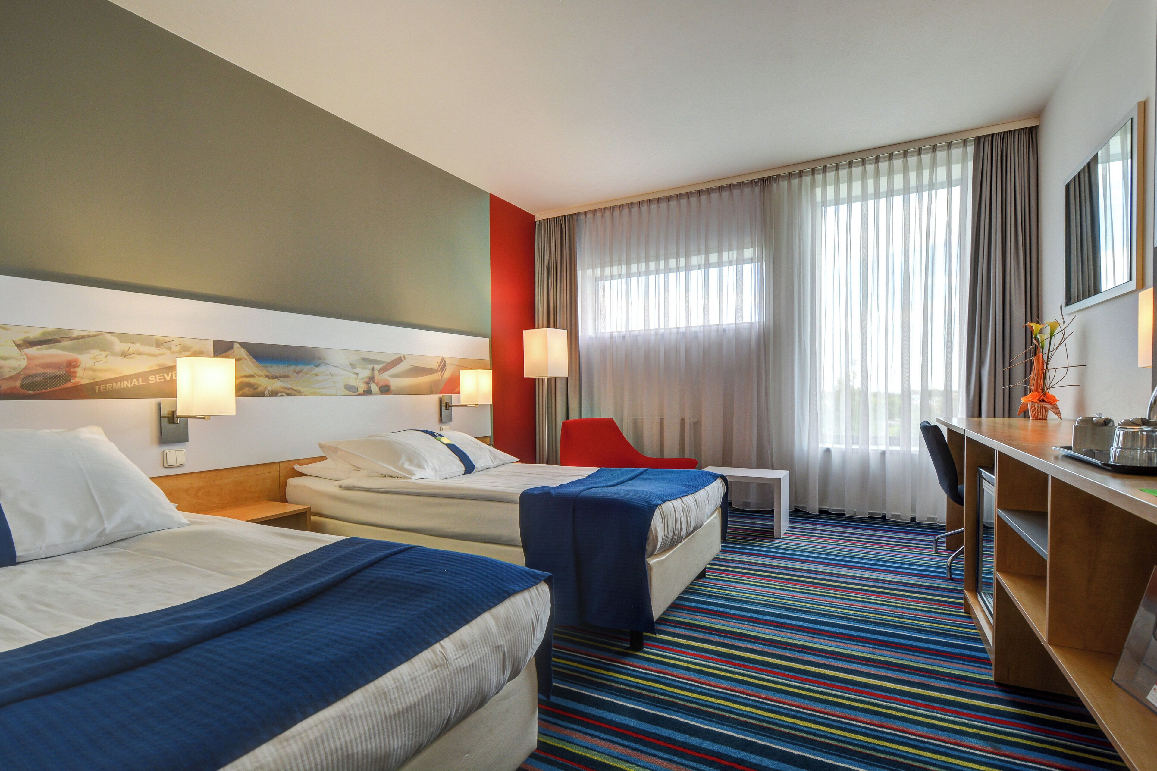 A hotel room with two beds, a desk, a chair, and a window with curtains.