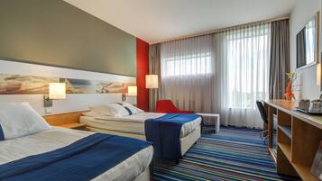 A hotel room with two beds, a desk, a chair, and a window with curtains.