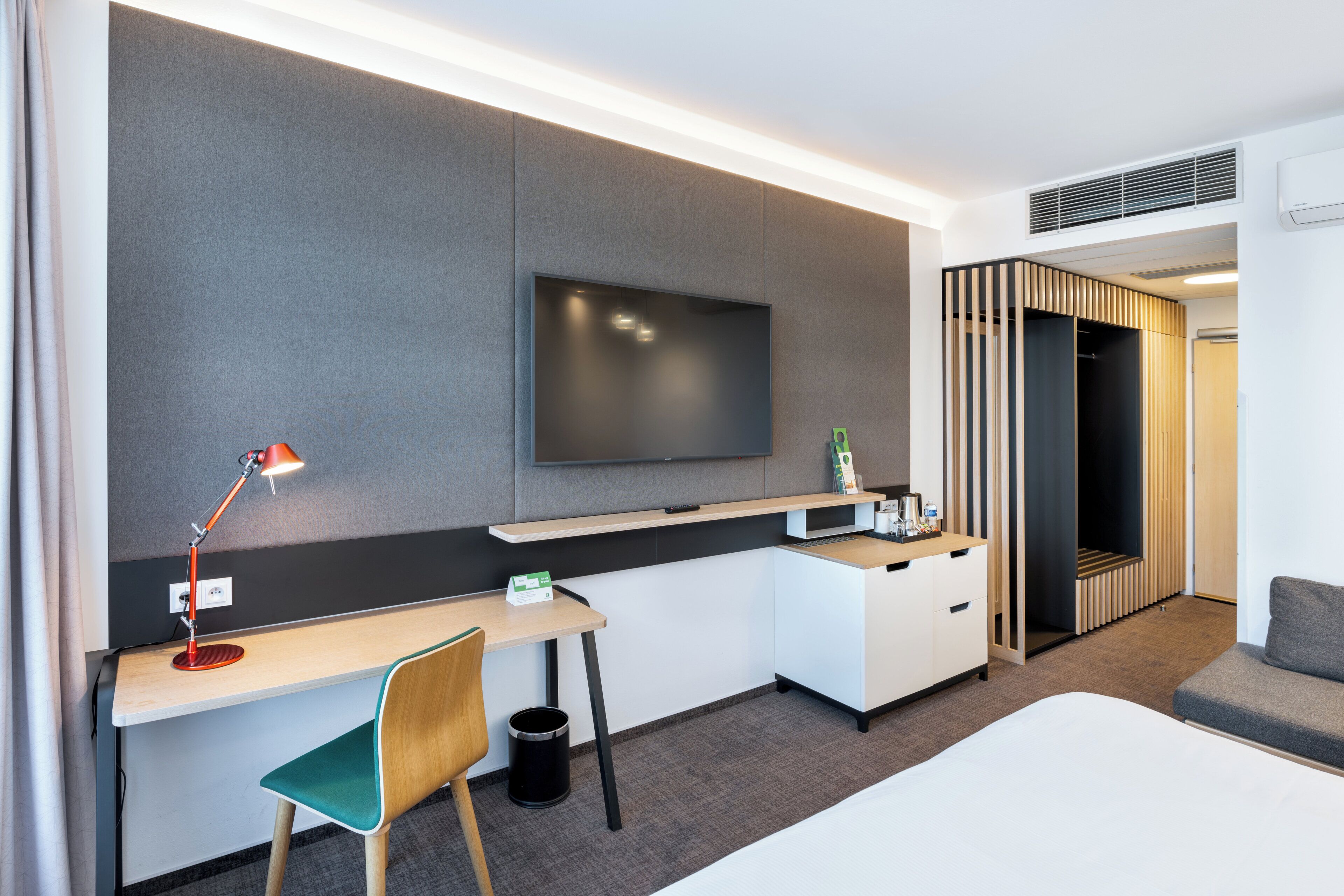 Een moderne hotelkamer met een flatscreen televisie aan de muur, een bureau met stoel, een bed en een inloopkast.