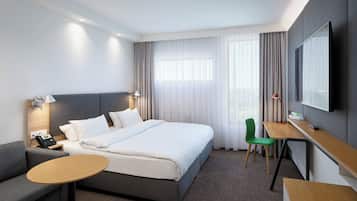 Ein Hotelzimmer mit Bett, Schreibtisch, Stuhl, Sofa und Fernseher.