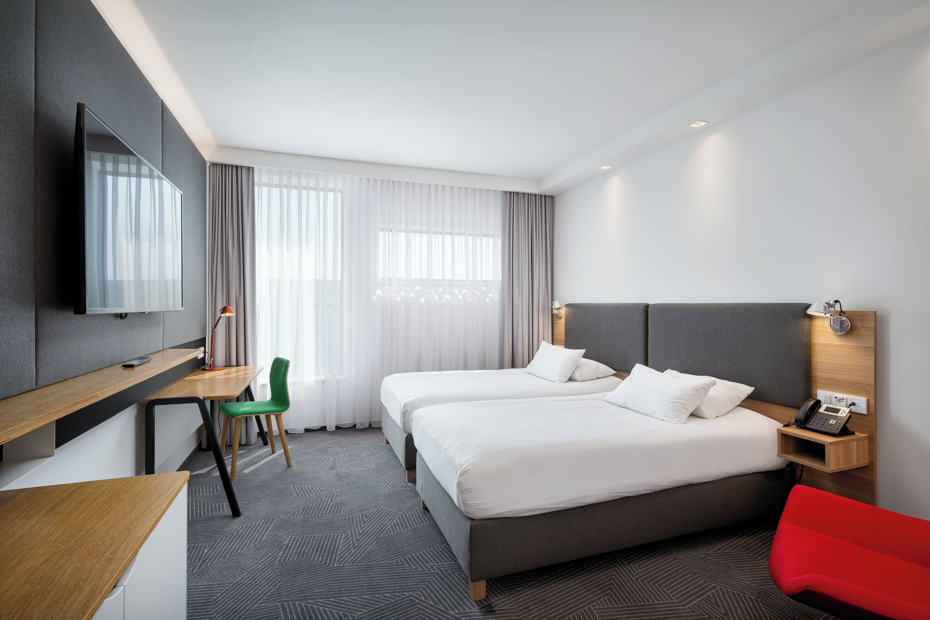 Ein Hotelzimmer mit zwei Betten, einem Schreibtisch, einem Fernseher und einem roten Sessel.