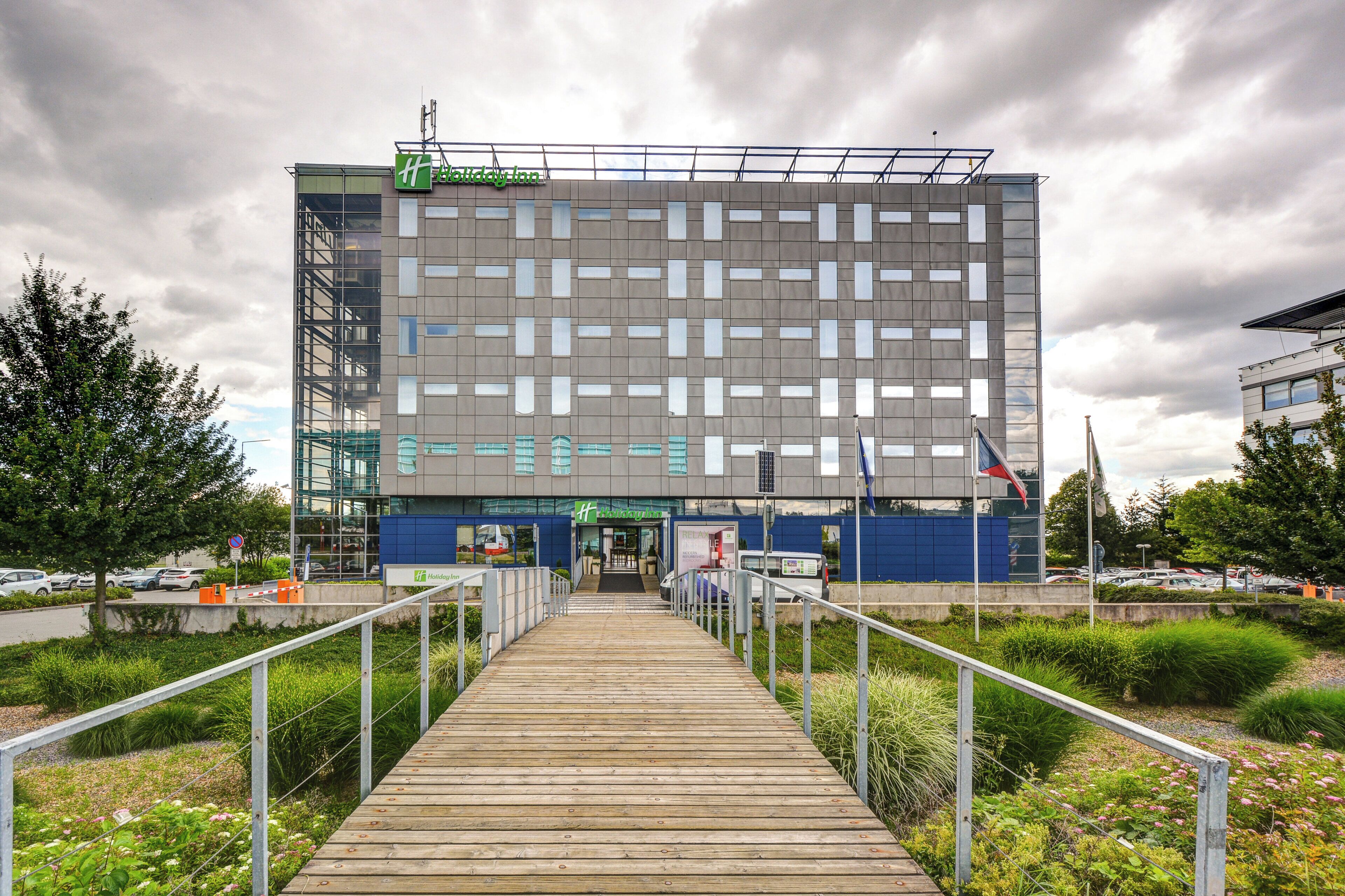 Ein modernes Holiday Inn mit einer markanten, geometrischen Fassade, einem hölzernen Wegweiser zum Eingang und einem Parkplatz im Hintergrund.
