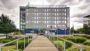 Ein modernes Holiday Inn mit einer markanten, geometrischen Fassade, einem hölzernen Wegweiser zum Eingang und einem Parkplatz im Hintergrund.