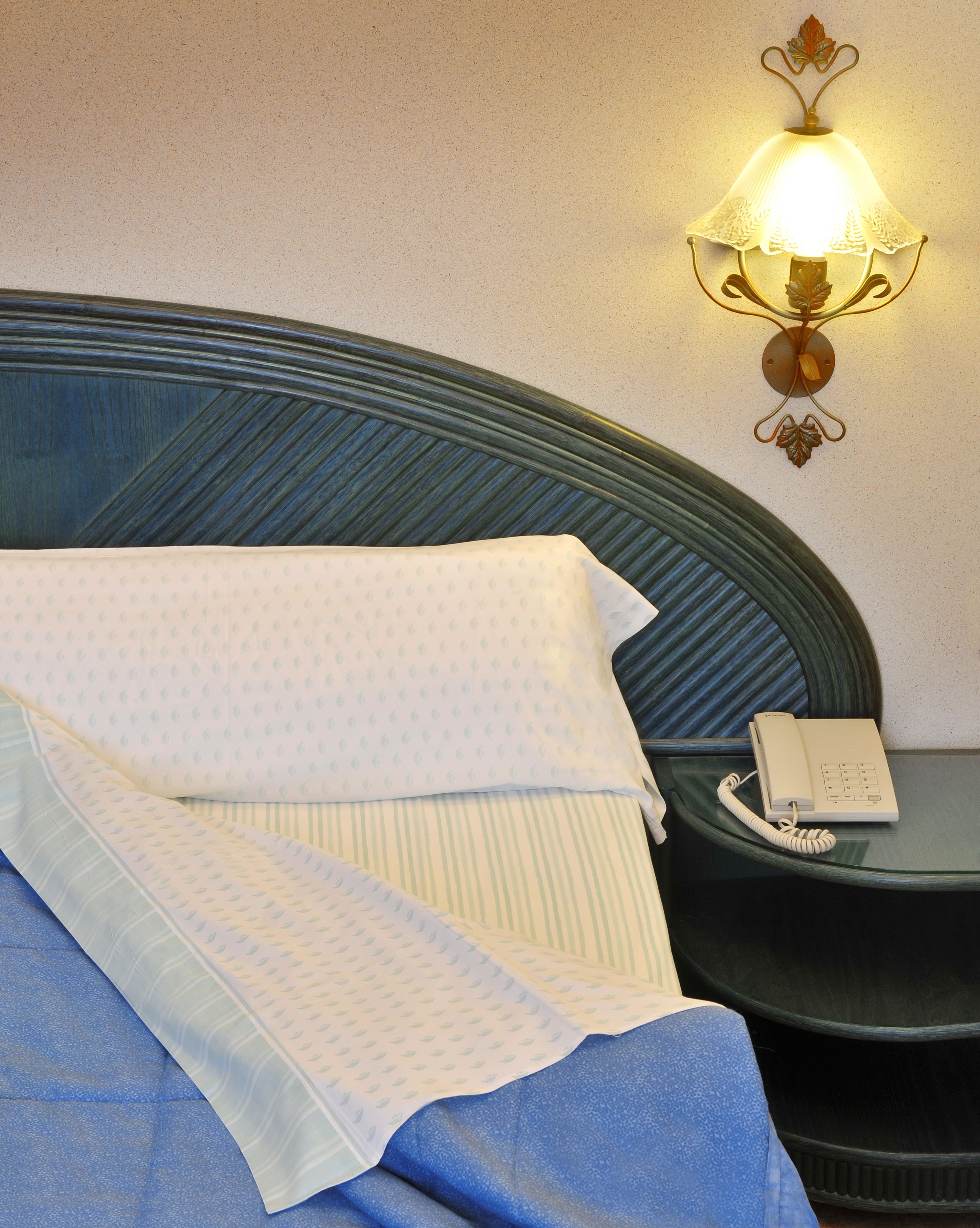 A neatly made bed with a patterned blanket, a bedside telephone, and a wall-mounted light fixture.