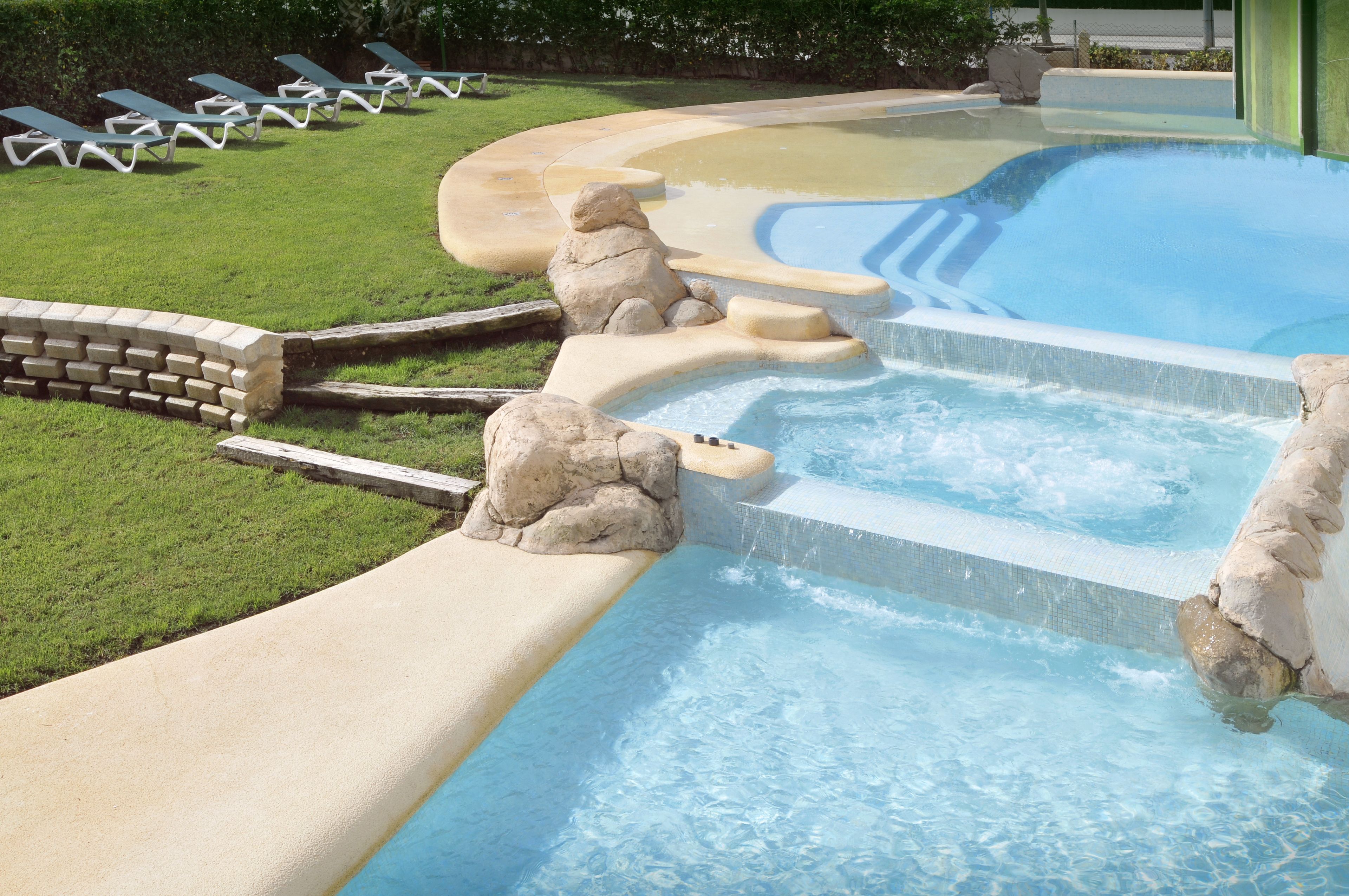 Une piscine agrémentée d’une cascade, de chaises longues et d’un mur en pierre.