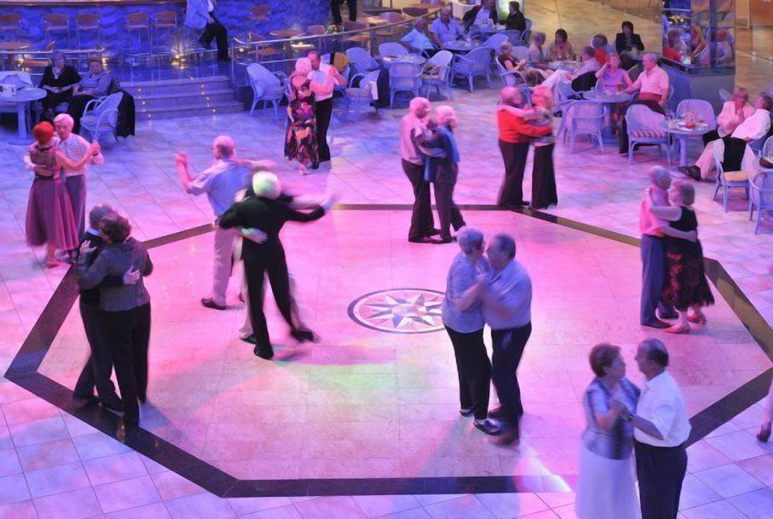 Um evento social numa sala ampla com um salão de dança central rodeado por convidados sentados.