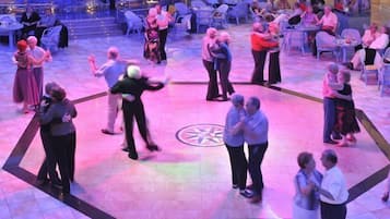 Um evento social numa sala ampla com um salão de dança central rodeado por convidados sentados.
