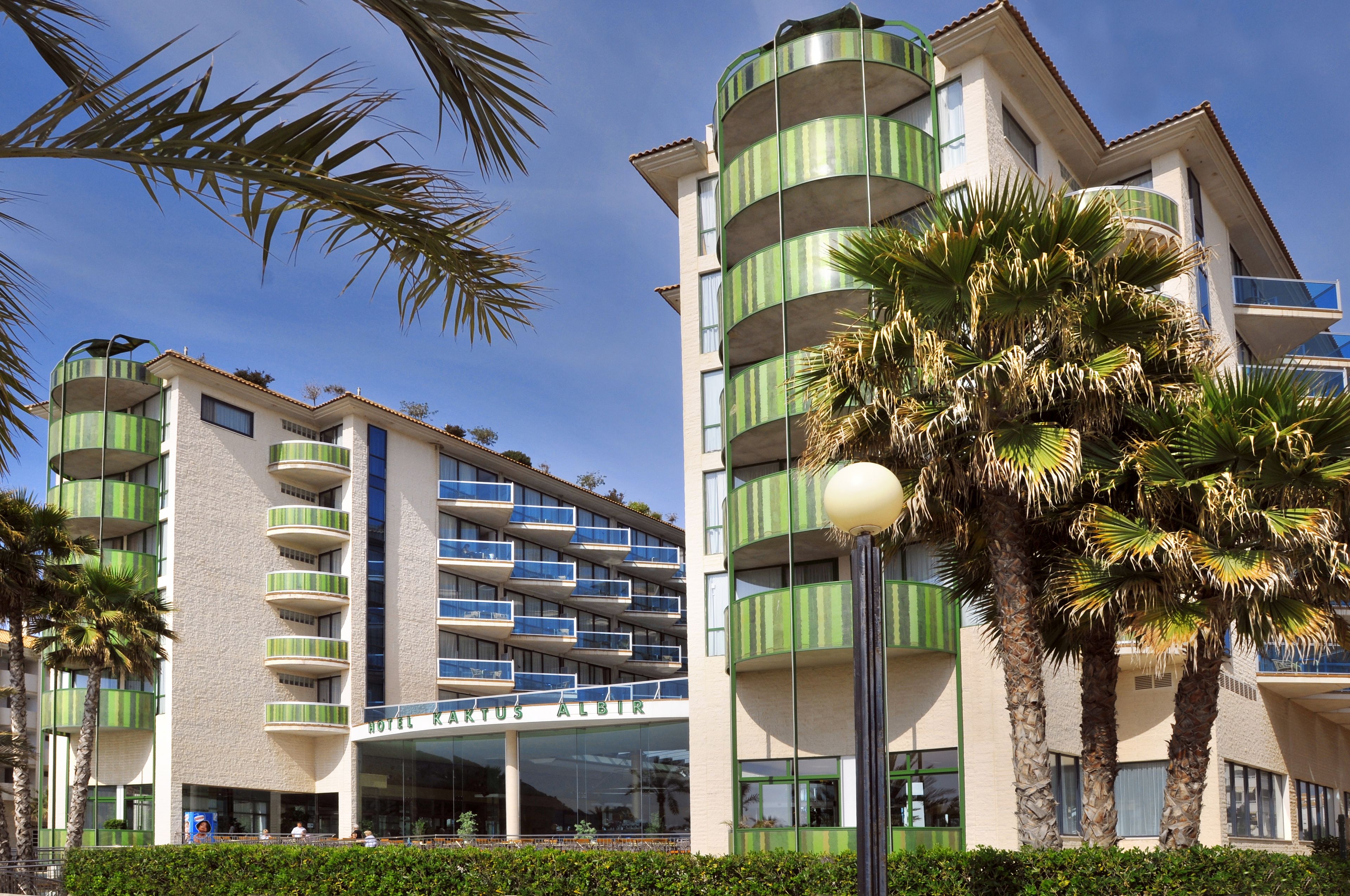 Un hôtel à plusieurs étages doté de balcons, de palmiers et offrant une vue sur un ciel dégagé.