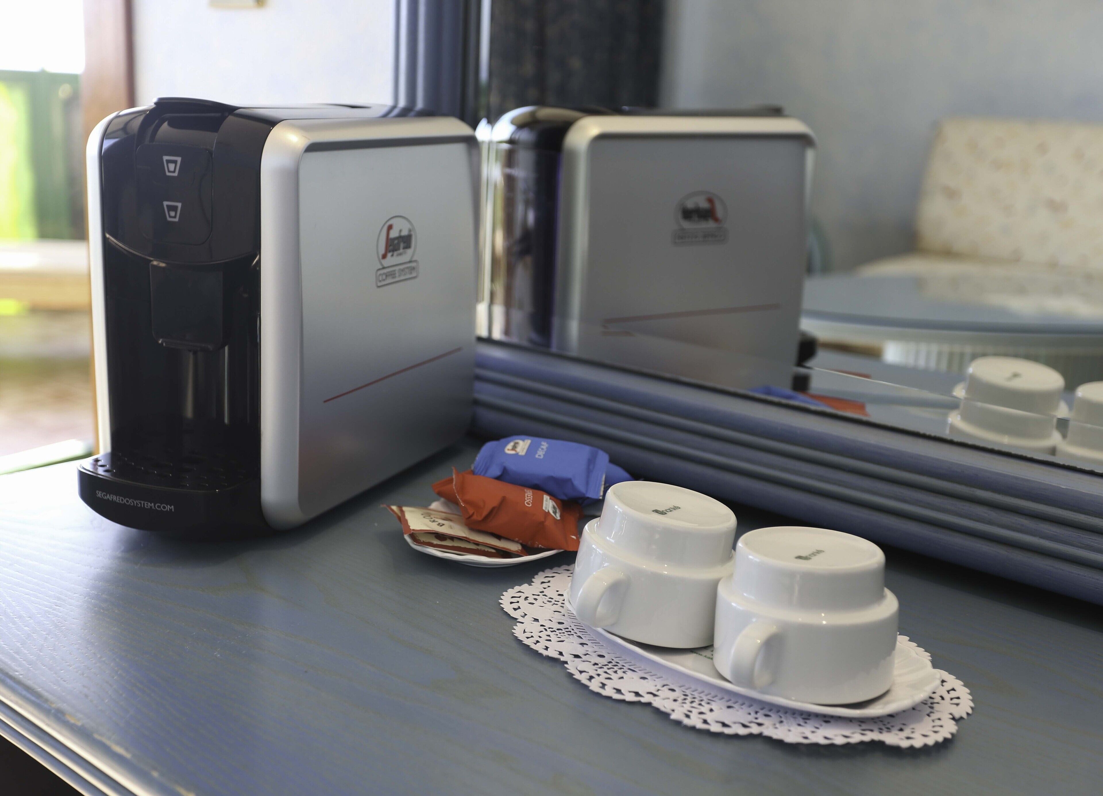 Une machine à café, une petite boîte et deux tasses sur une table recouverte d’un chemin de table.