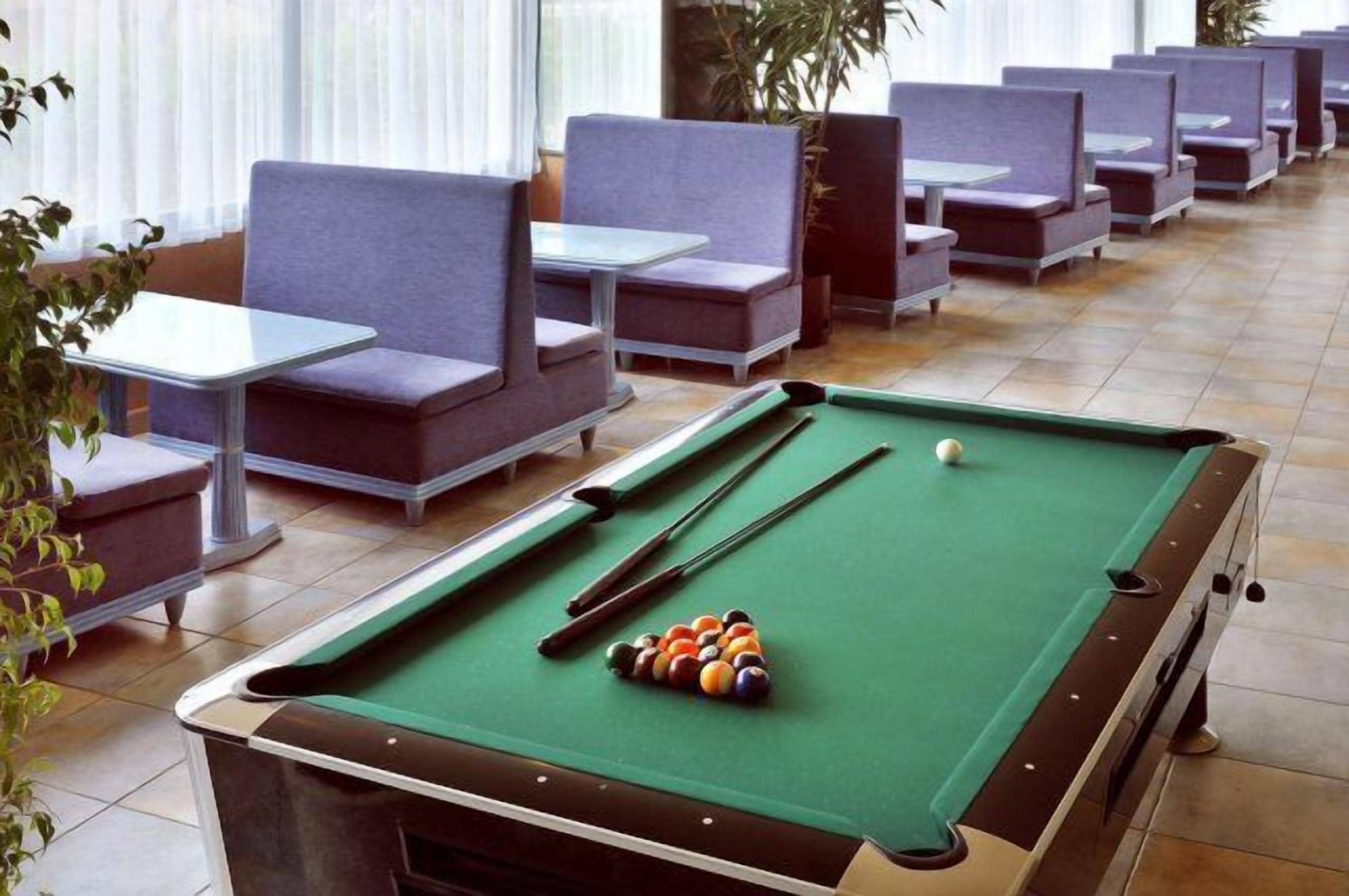 A pool table with balls and cues in a room with seating and a view of the outdoors.