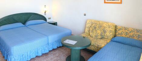 A room with two single beds, a small round table, a sofa, and a wall-mounted picture.