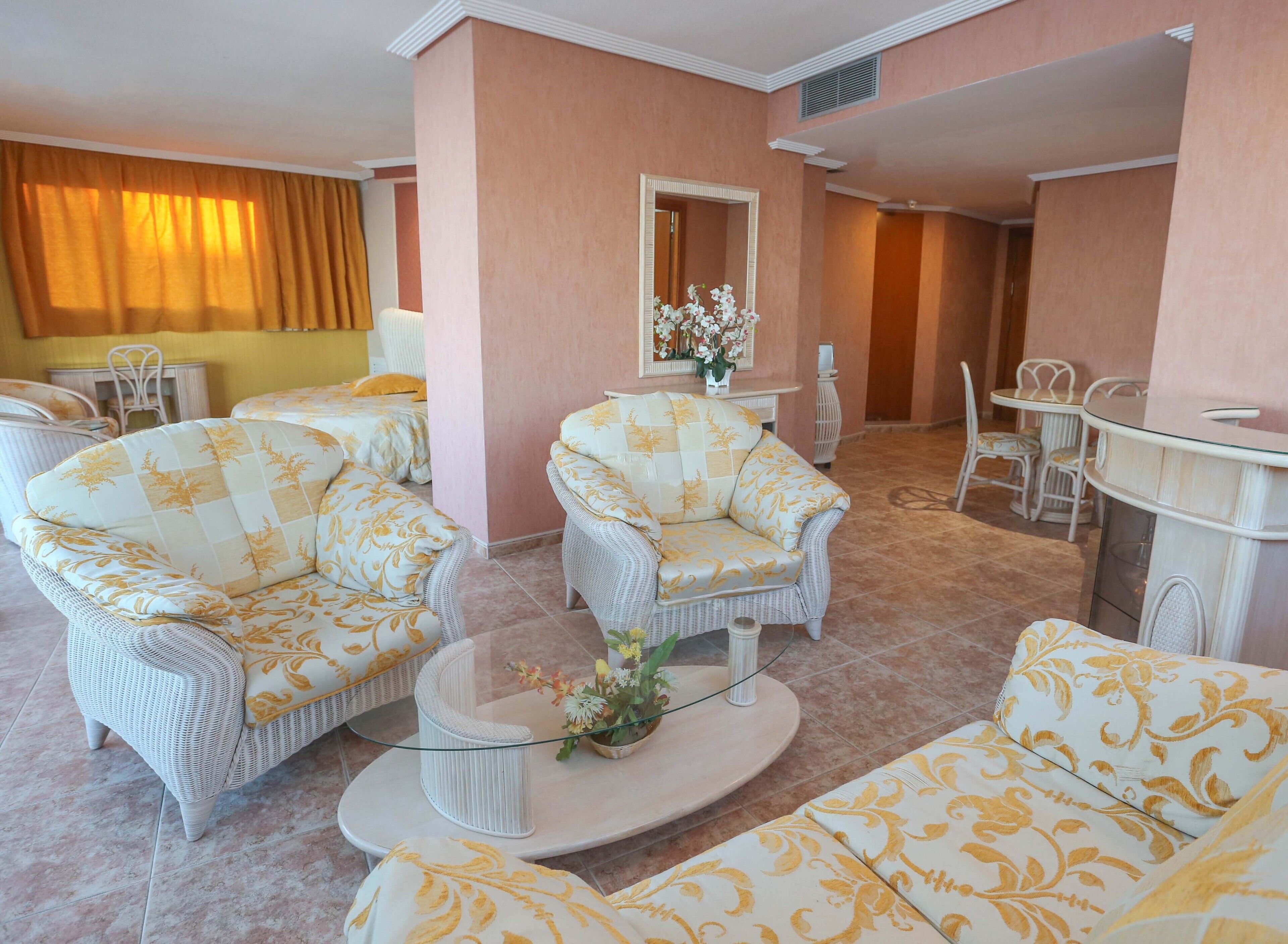 A hotel room with wicker furniture, a glass coffee table, and a mirror.
