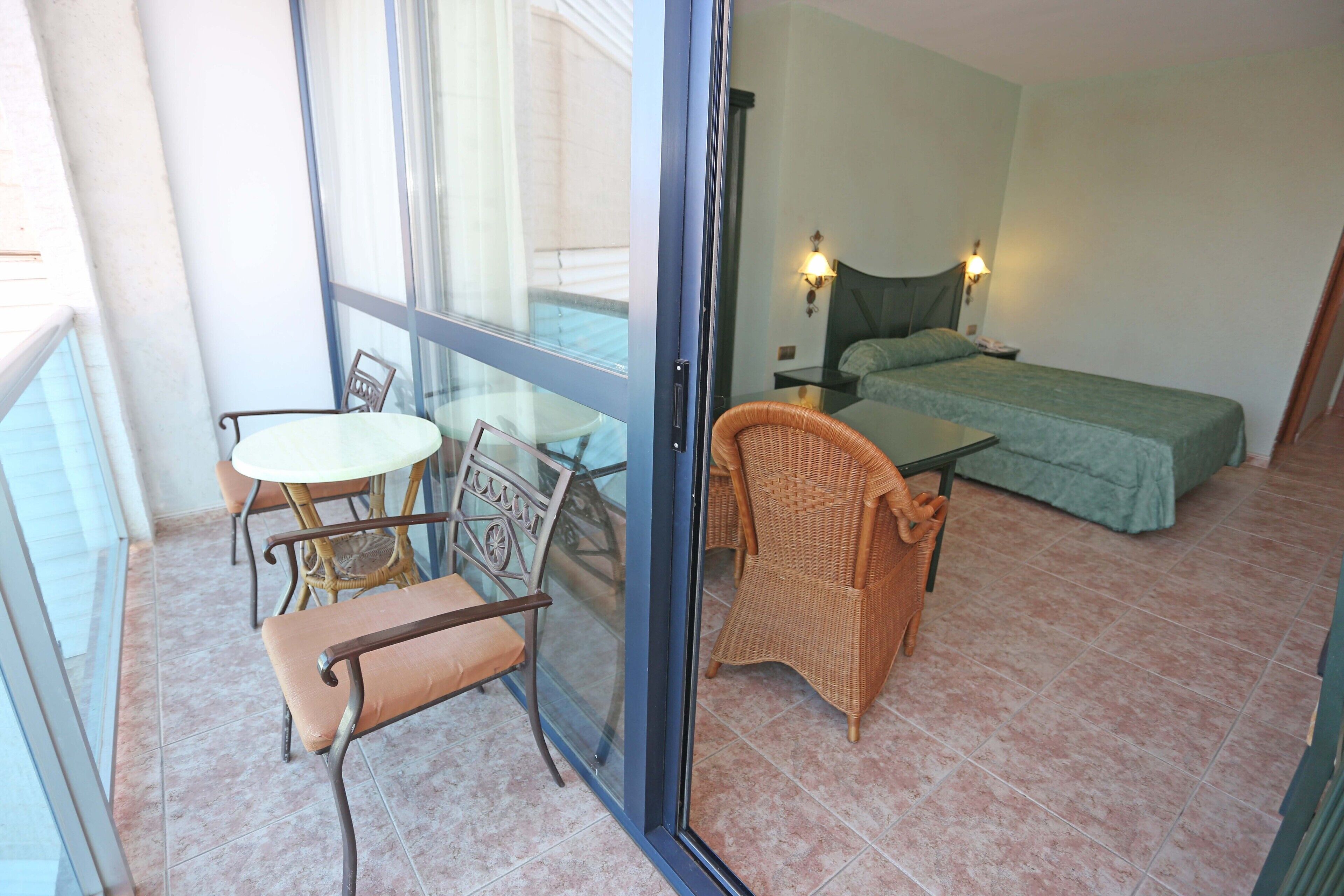 A balcony with wicker furniture, a bed with green bedding, and a nightstand with a lamp.