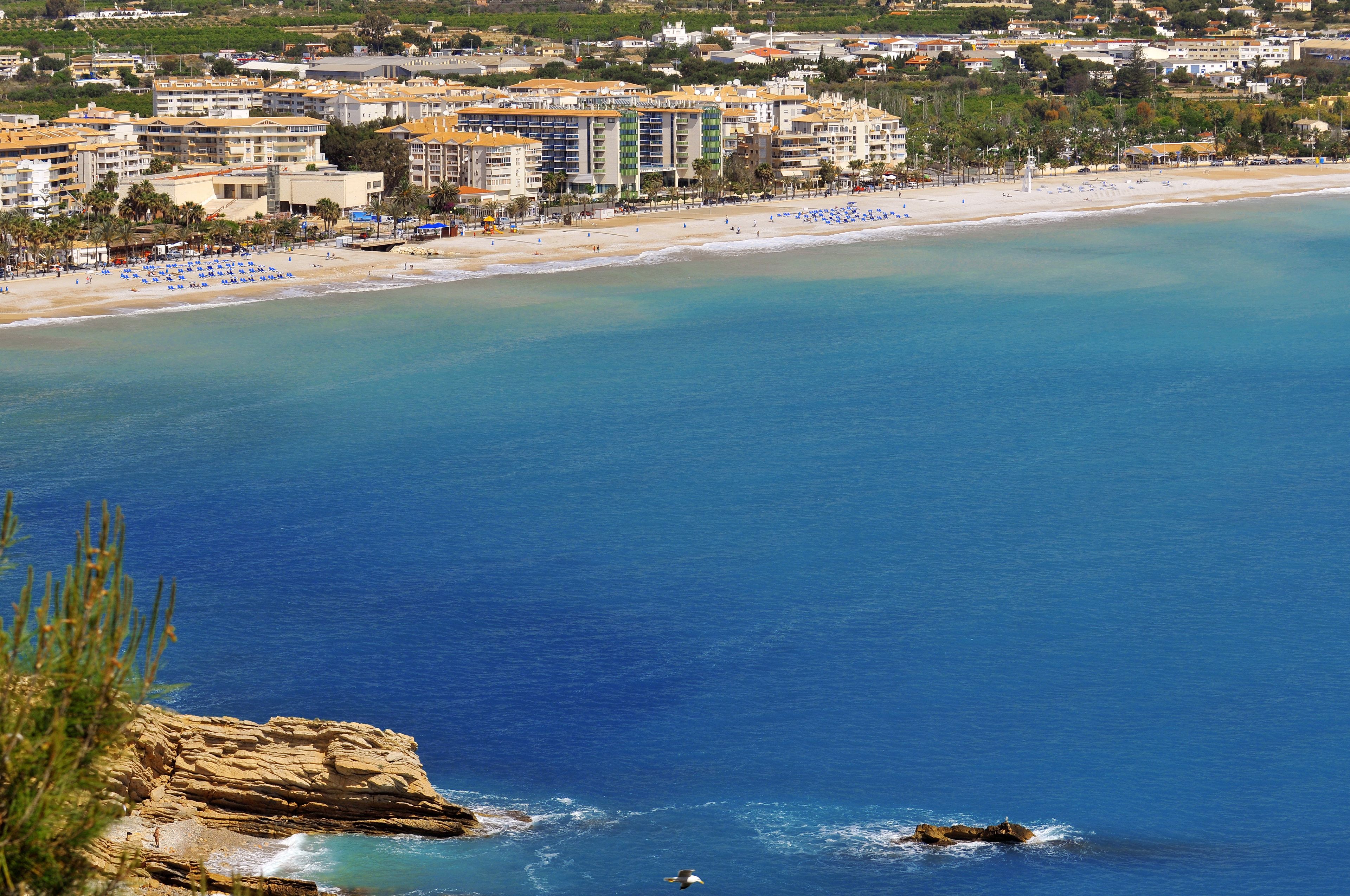 A coastal hotel with multiple buildings, a beach, and a rocky shoreline.