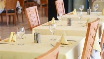 A restaurant with neatly arranged tables, each set with a folded napkin, a wine glass, cutlery, and a salt and pepper shaker.
