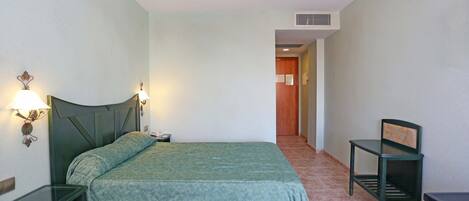 A hotel room with a bed, bedside tables, a chair, and a desk.