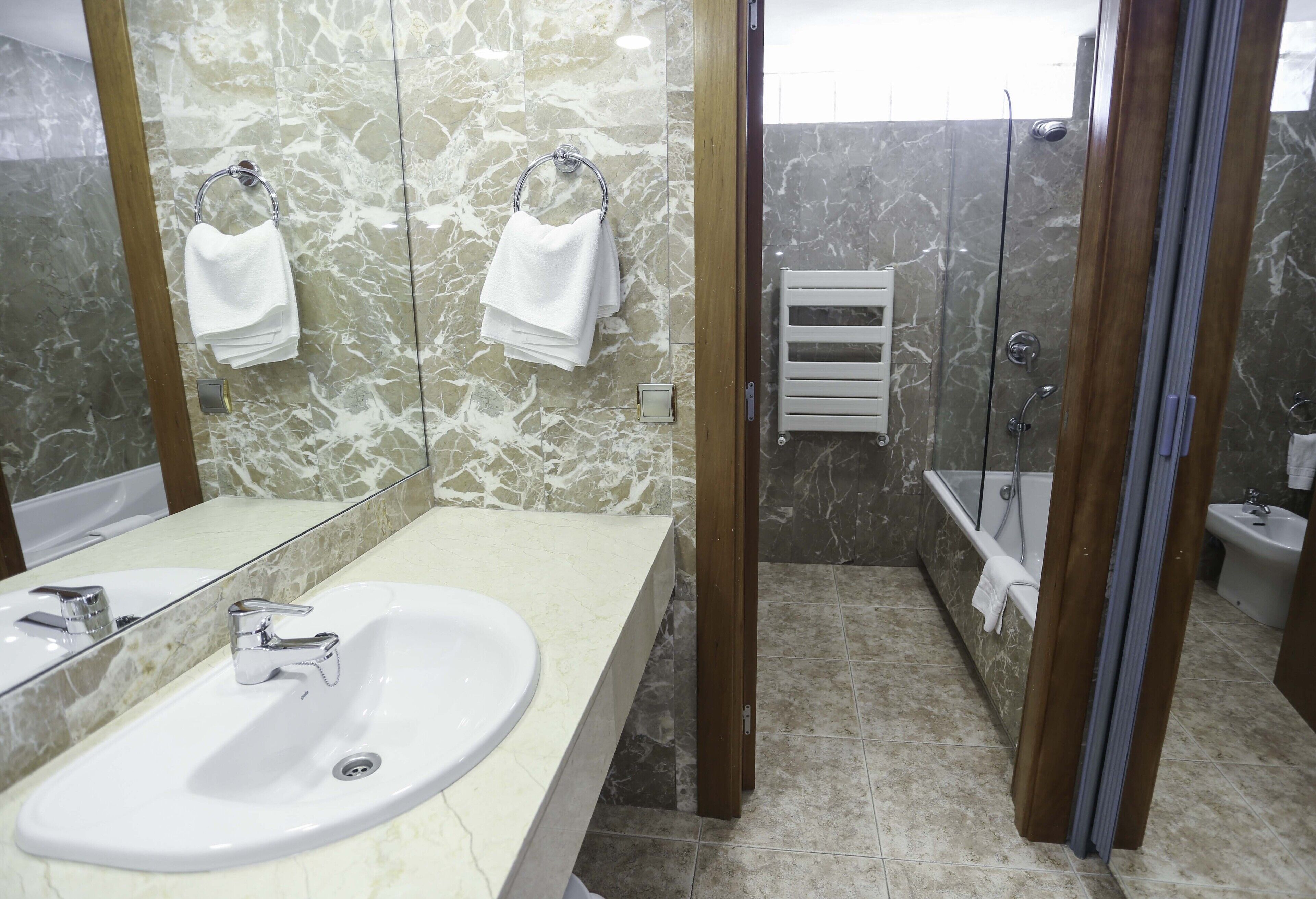A bathroom with a marble sink, a mirror, a shower, and a bathtub.