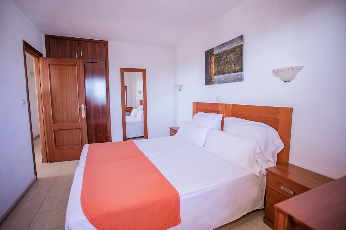 A bedroom with a large bed, wooden wardrobe, and a bedside table.