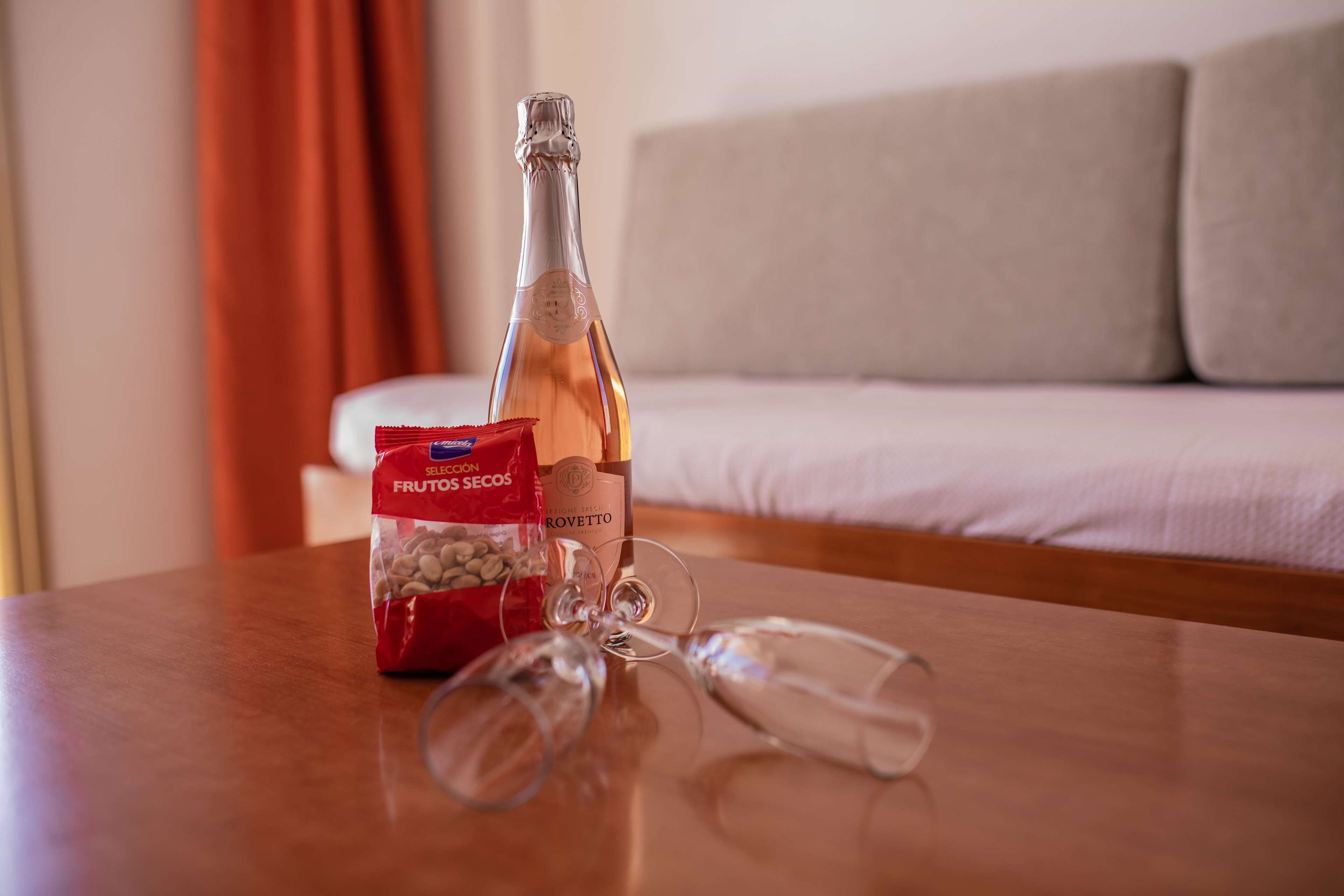 Eine Champagnerflasche, eine Nussmischung und zwei Gläser auf einem Holztisch in einem Raum mit einer Couch.
