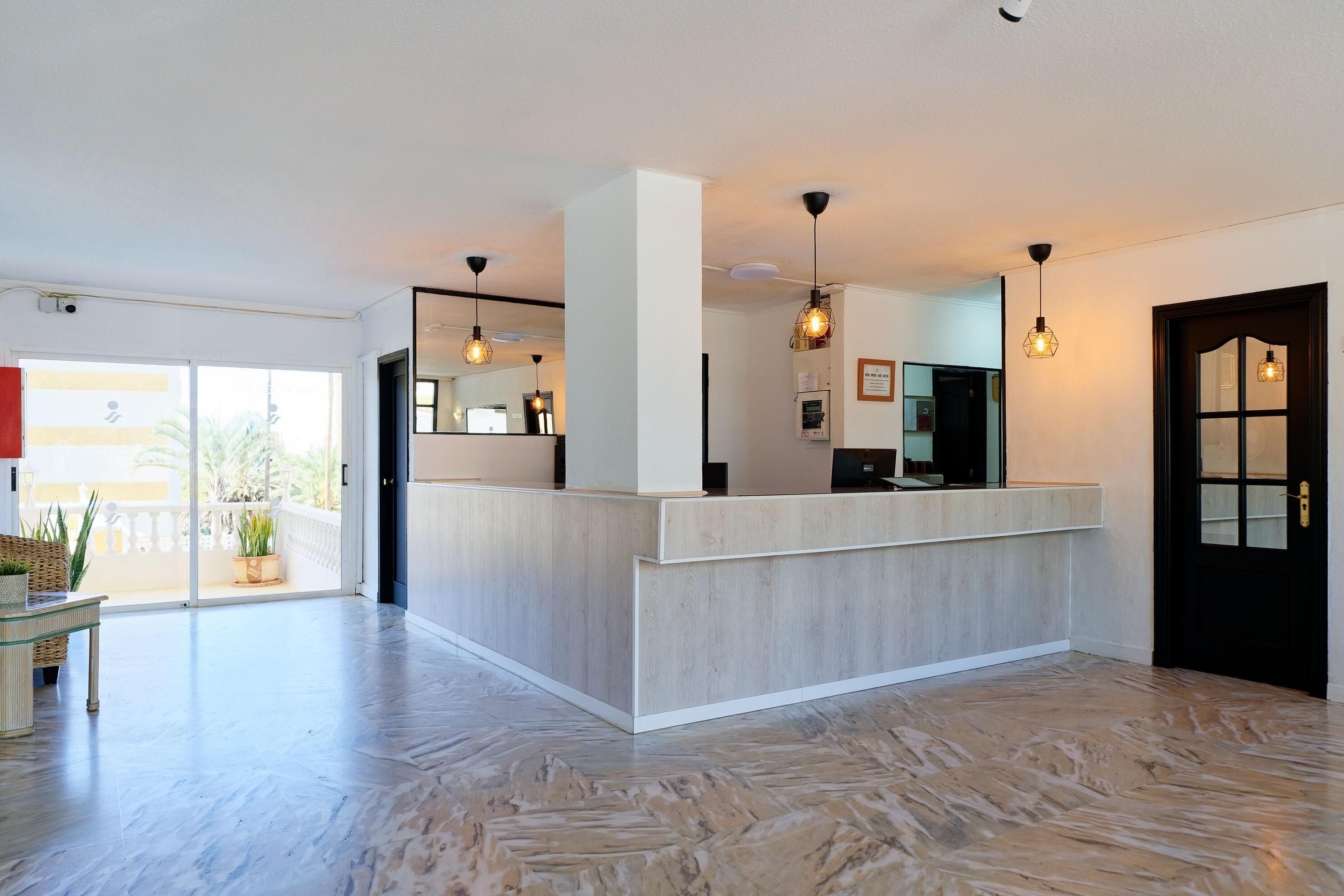 A modern hotel lobby with a reception desk, large windows, and a herringbone floor pattern.