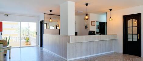 A modern hotel lobby with a reception desk, large windows, and a herringbone floor pattern.