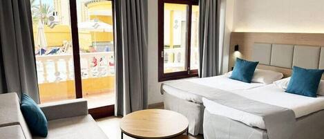A hotel room with a bed, a sofa, a small round table, and a balcony with a view.