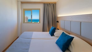 A hotel room with two beds, a view of the sea through a window, and a wooden headboard. - Servatur Caribe (Adeje)