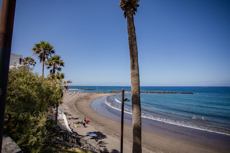 Una playa cerca, arena negra, sillas reclinables de playa, sombrillas