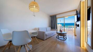 A modern living room with a sofa, chairs, a table, and a large window with a view of the sea.