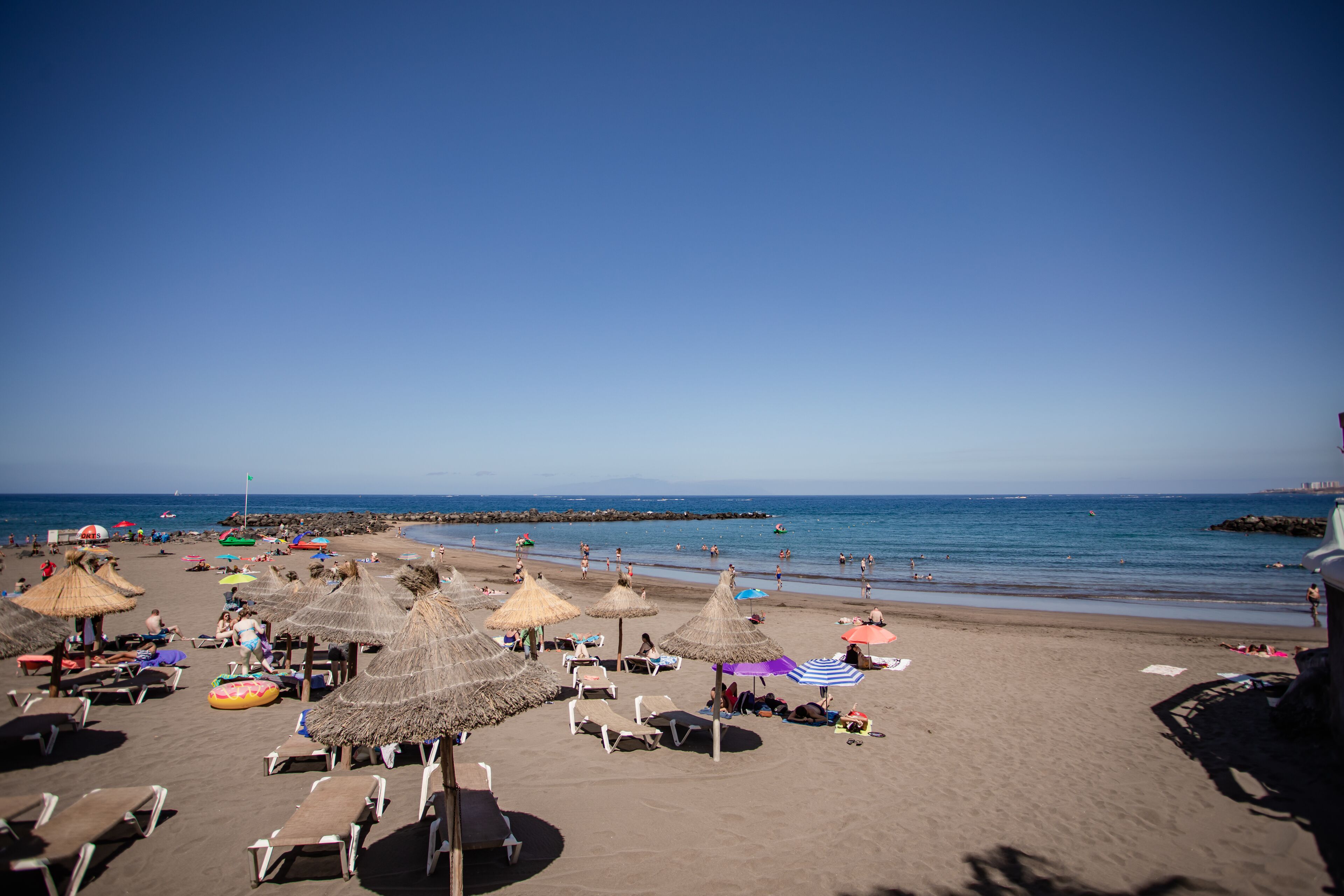 Une plage avec des parasols en chaume, des chaises longues et une vue dégagée sur la mer.