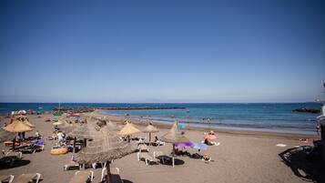 A beach with thatched umbrellas, lounge chairs, and a clear view of the sea.