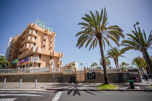 Un hotel llamado "Aptos Caribe" con un diseño arquitectónico moderno, palmeras y un cielo azul despejado.