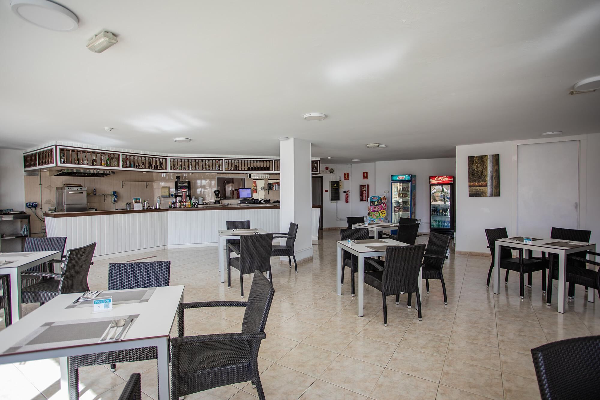 A restaurant with a bar area, tables, chairs, and a kitchen in the background.