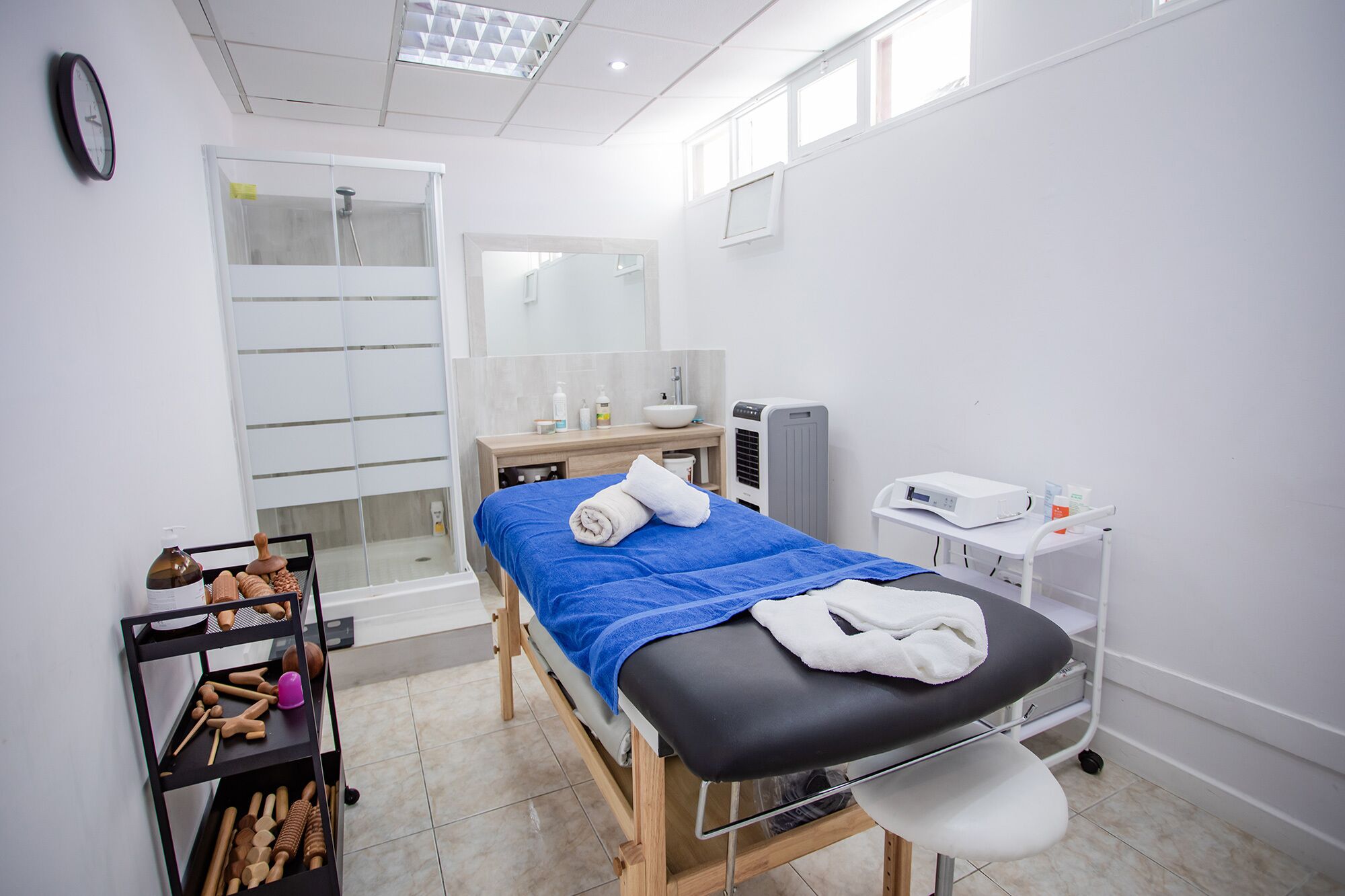 A clinical setting with a treatment bed, a sink, a mirror, and a shelf with medical tools.