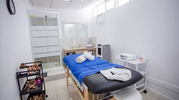Um ambiente clínico com uma cama de tratamento, pia, espelho e prateleira com instrumentos médicos.