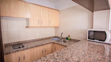 A kitchen with granite countertops, wooden cabinets, a stainless steel sink, a microwave, and a dish soap bottle.