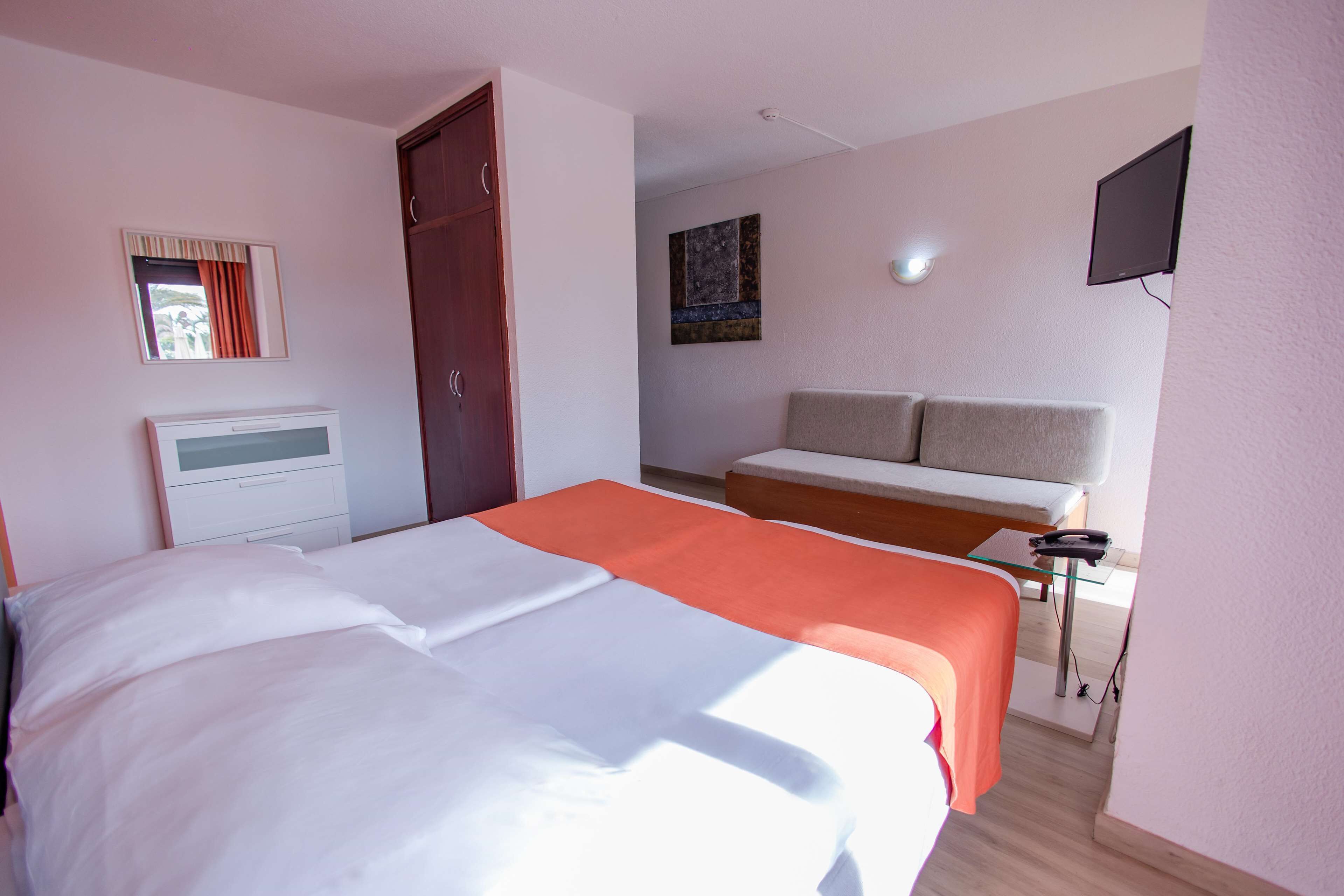 Una habitación de hotel con cama, sofá, televisión y ventana con cortinas.