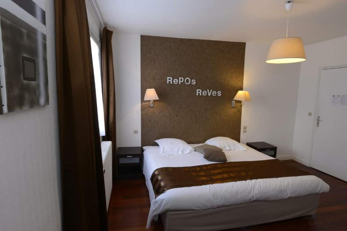 Ett hotellrum med en säng, en sänggavel med texten ”Repos Reves”, två sänglampor, ett nattduksbord och en dörr.