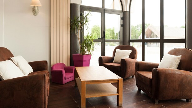 A modern living room with brown leather sofas, a wooden coffee table, and a large window with a view of greenery outside.