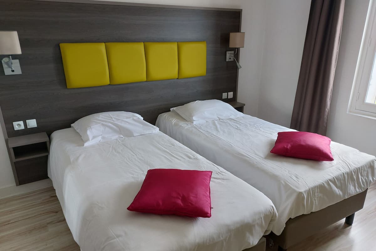 Ett hotellrum med två sängar, en sänggavel i trä och en accentpanel i en stark gul färg.