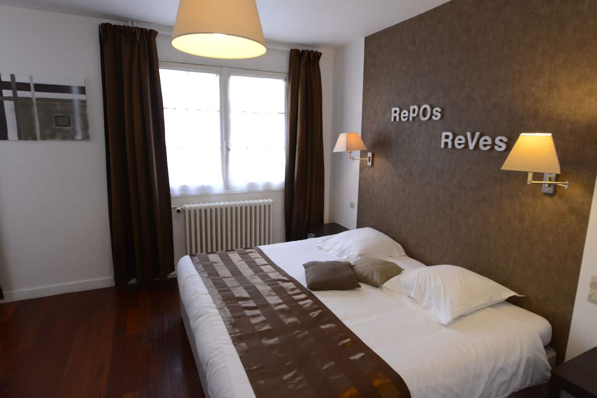 Ett hotellrum med en säng, två sänglampor, ett fönster med gardiner, ett element och en skylt som är monterad på väggen.