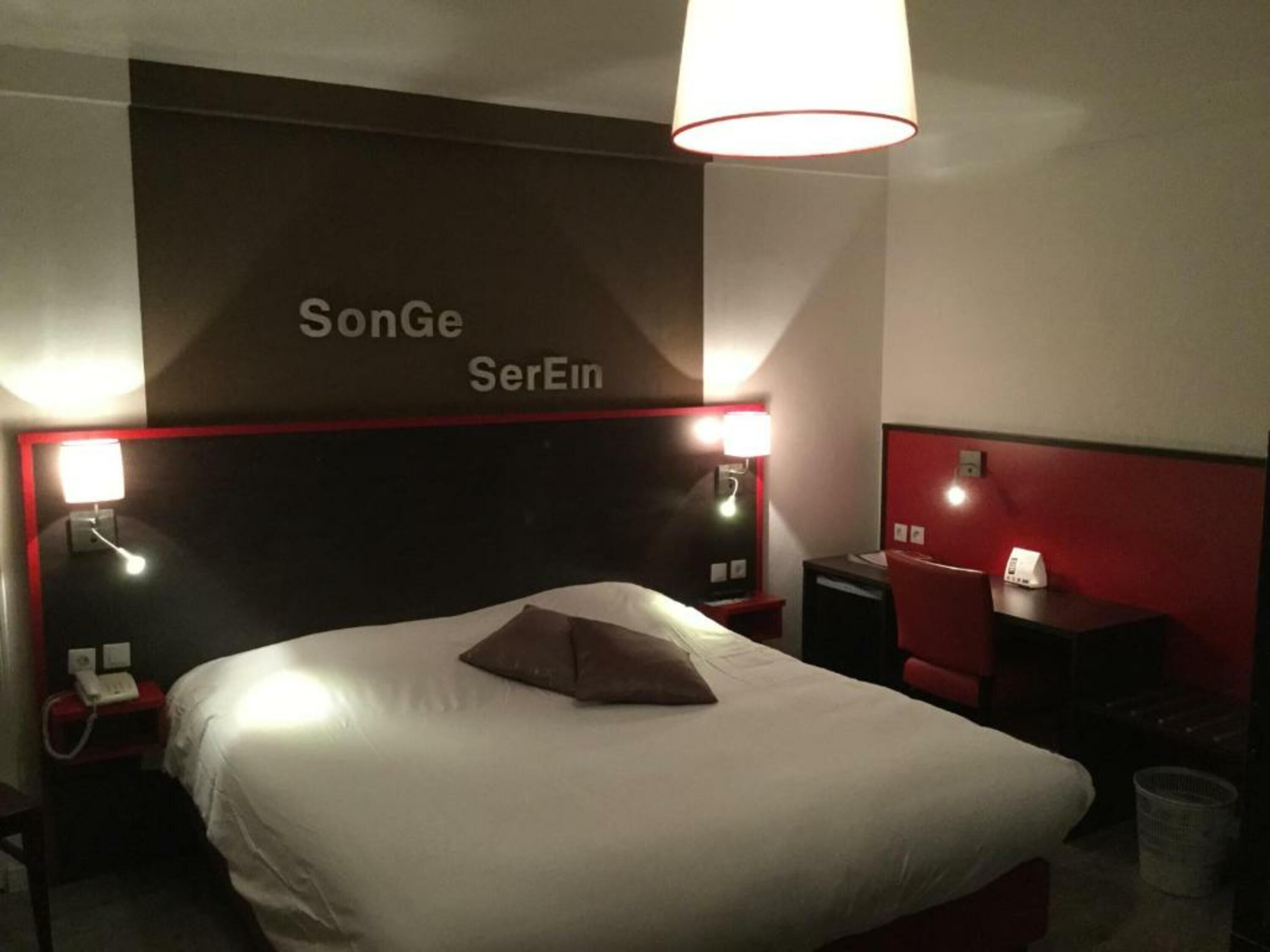 Habitación de hotel con una cama grande, una pared de acento roja y un cartel sobre la cama que dice 'SonGe SerEin'.
