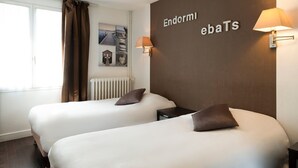 A hotel room with two beds, a brown wall with the name 'Endormi ebaTS', a window with curtains, and a wall-mounted lamp.