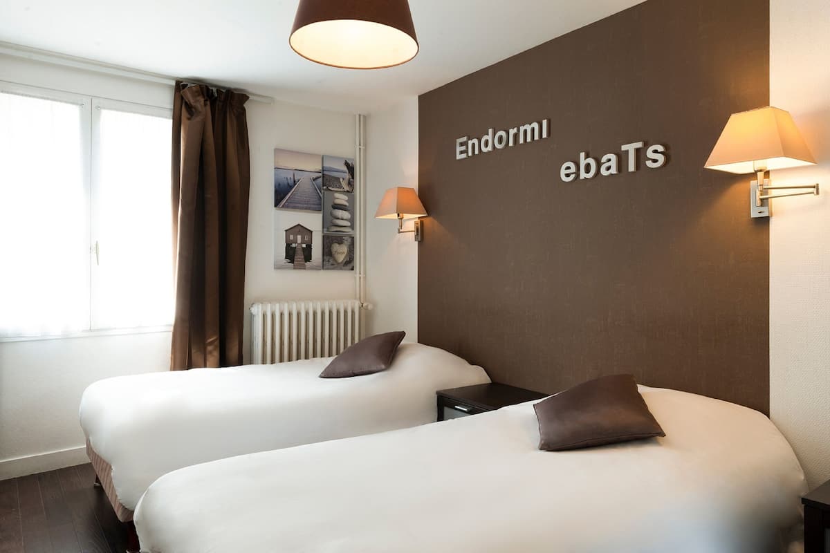 Ett hotellrum med två sängar, en brun vägg med namnet ”Endormi ebaTS”, ett fönster med gardiner och en vägglampa.