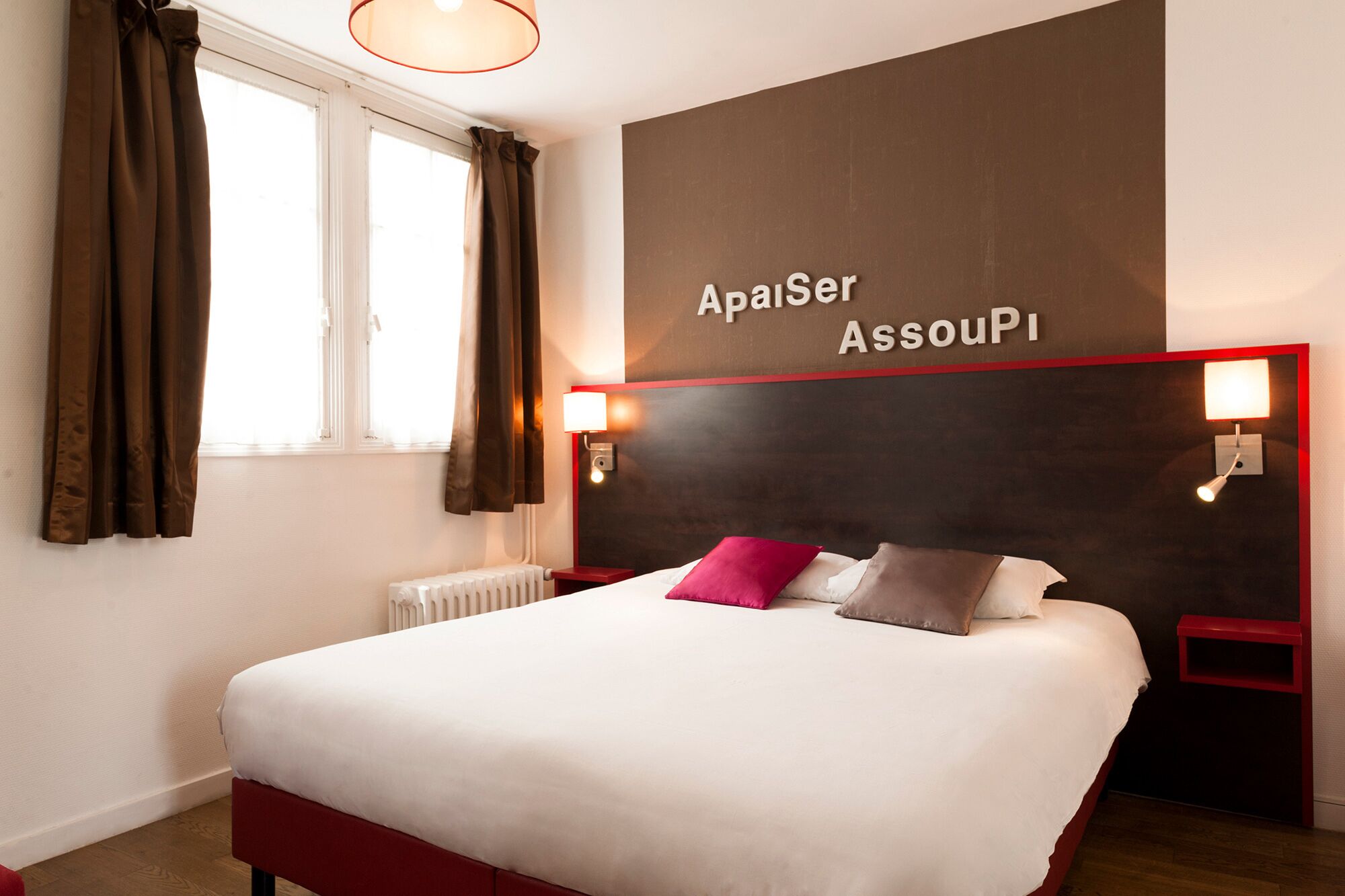 Una habitación de hotel con una cama grande, cortinas marrones, un cartel en la pared que dice "Aposer AssouPI" y dos lámparas de noche.